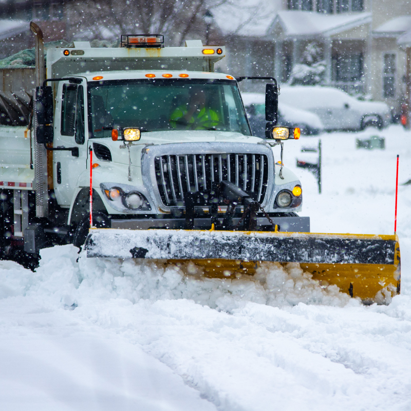 Front view of snow plow truck with yellow push blade clearing covered roads after heavy winter snow